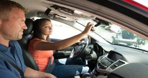 Student driver adjusts rear-view mirror with teacher watching from the passenger seat. | Ellisville, MO