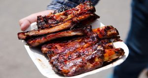 Hand holding a white plate with barbecue ribs on it. | Tacoma, WA