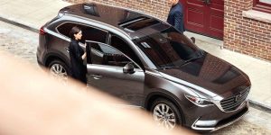 A woman and a man opening the the front doors of a silver 2019 Mazda CX-9 preparing to get in. | Mazda dealer in Ellisville, MO