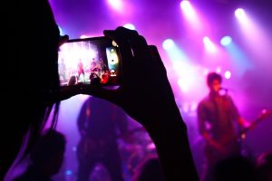 Close of a person's hands holding a phone recording the stage of a music group performing live. 