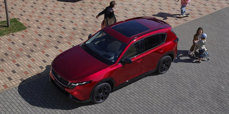 A red Mazda CX-5 SUV parked on a paved area with people walking nearby.