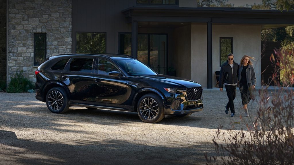 A Mazda CX-70 SUV parked in front of a house with a couple walking beside it.