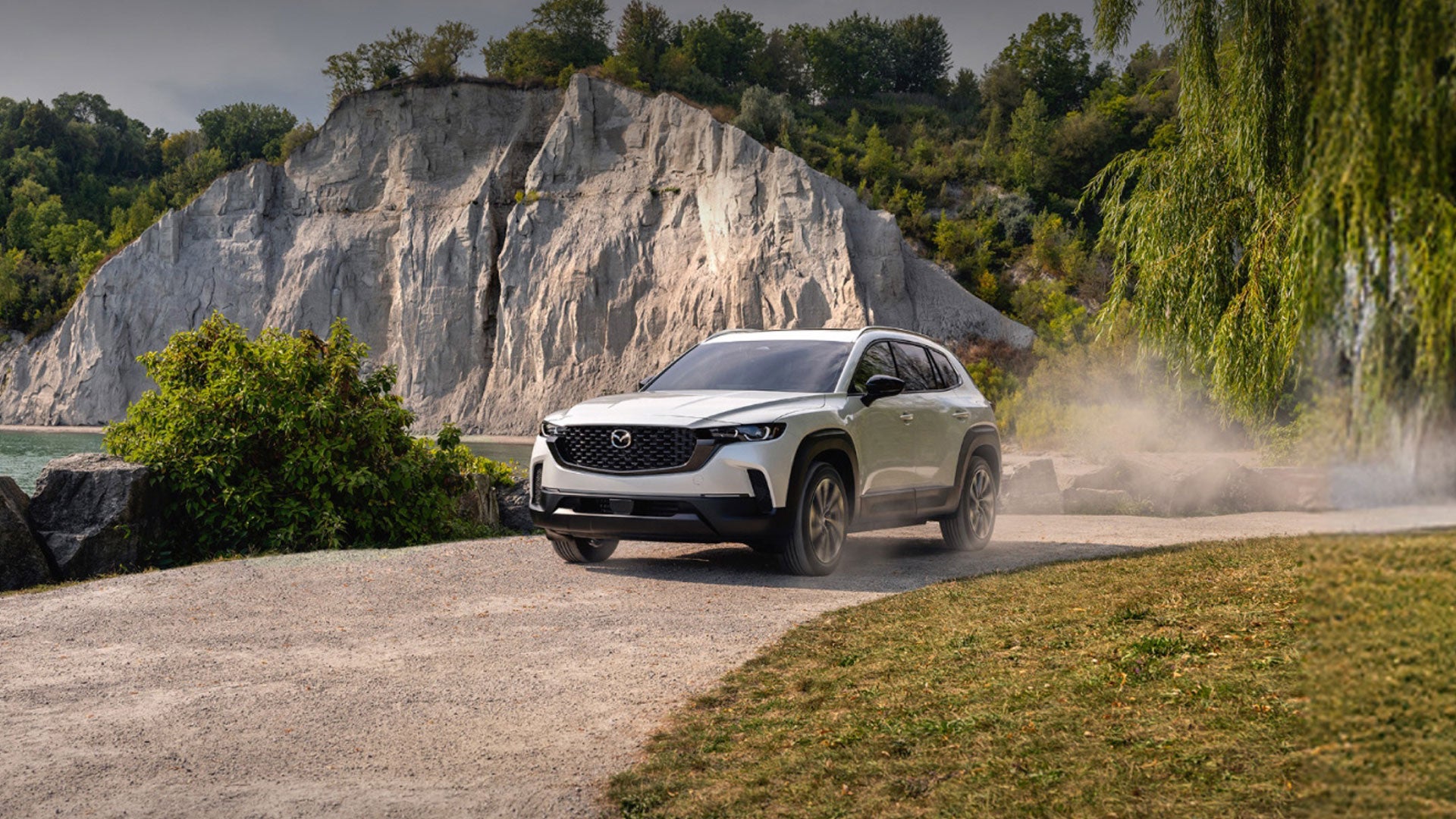 White Mazda CX-50 SUV driving along a rocky mountain road.